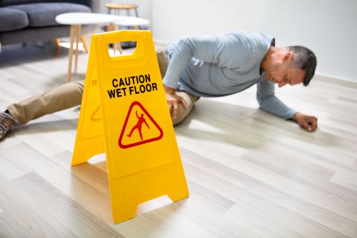 A man slips next to a caution wet floor sign.
