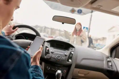 A distracted man is using his phone while driving right before hitting a woman crossing the street. 