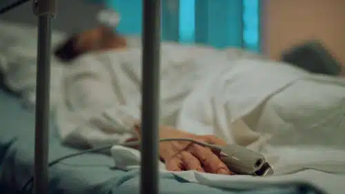 A male patient lies in a hospital bed in a coma.