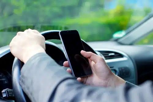 A close up of a man's hands using a cell phone while driving distracted in Georgia.