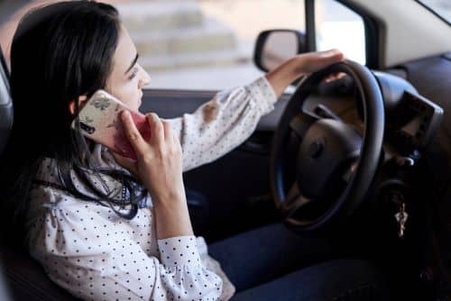 A female distracted driver operates her car while using the phone.
