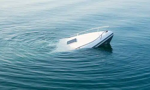 A white boat sinking in a freshwater lake with its bow just above the water level.