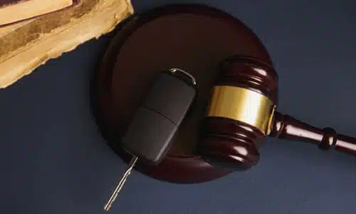 A judge's gavel and a car key resting on top of a sound block, and with two books stacked on top of each other nearby.
