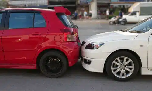 A side view image of a white car having rear-ended a red hatchback in the middle of the road.