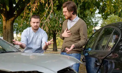Two men arguing on a suburban road over whose fault the car collision was.