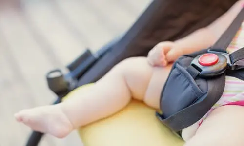 A closeup of a car seat lock holding a baby in place in the back seat of a car.