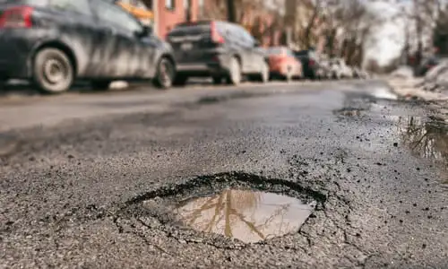 A low shot of a pothole in a city street next to a row of parked cars.