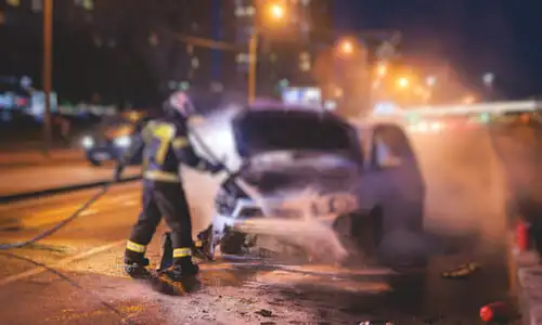 Firefighters putting out a car battery fire on a city road at night.