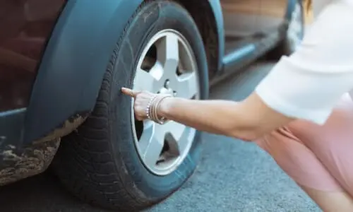 A woman touching the flat tire of her car that caused her accident and left her stranded.