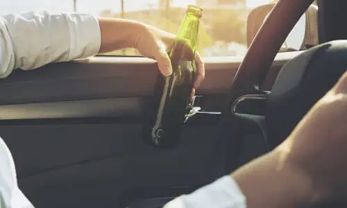A man holding a bottle of beer in one hand while driving.