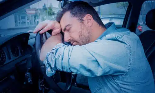 An exhausted driver asleep at the wheel of his car.