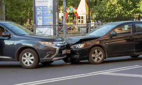 A head-on collision between two black vehicles on a city street.