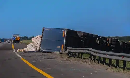 An overturned heavy truck with unsecured cargo spilled out of the transport container.