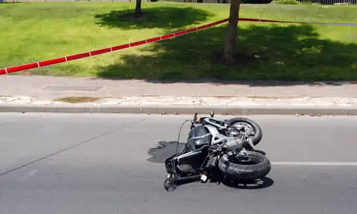 A motorcycle is on its side after an accident, red police tape surrounds the scene.