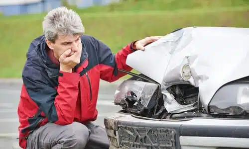 An upset car owner looking at damage dealt to his vehicle by a hit and run driver.