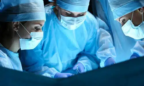 Three doctors in a surgical theater performing invasive surgery on a patient.