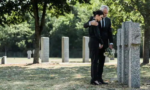 Two people standing at a wrongful death victim's grave after a funeral, mourning.