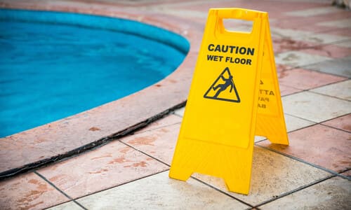 A yellow wet floor warning sign standing next to a swimming pool.