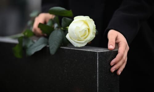 A woman's hands resting on a black granite tombstone mourning over a lost loved one.