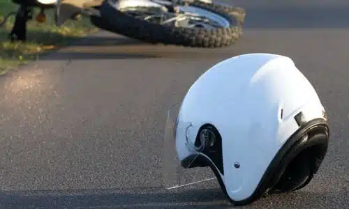 A white helmet on a road with a crashed motorcycle in the background.