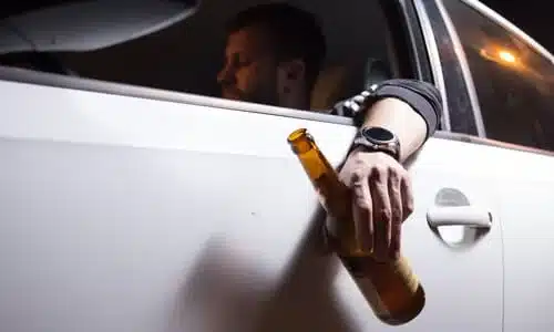 A drunk driver holding a beer bottle in his hand while driving down the highway.
