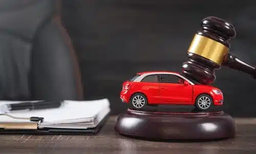 A judge's gavel striking a red miniature car resting on a soundblock.