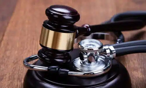 A gavel with a stethoscope wrapped around it, resting on a soundblock in a courtroom.