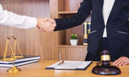 A personal injury lawyer shaking a client's hand in his office. 