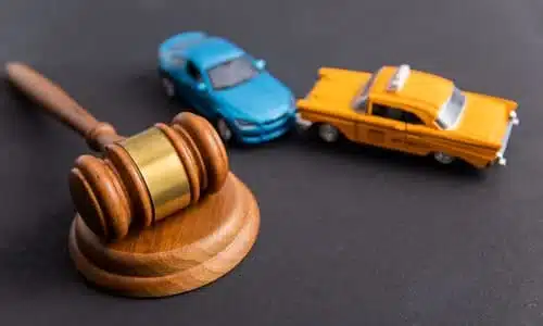 A gavel and soundblock on a felt surface, with a miniature car and a cab depicting a collision in the background.