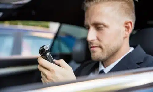 A man in the driver's seat of his car looking at a breathalyzer he is about to use.