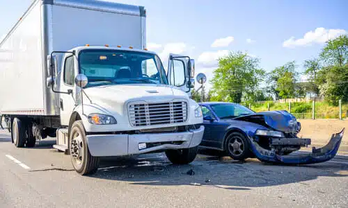 A white semi truck and a dark blue car on a highway after an accident where they collided with each other.