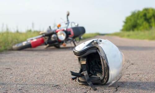 A red motorbike tipped on its side after an accident, with a white helmet on the road in the foreground.