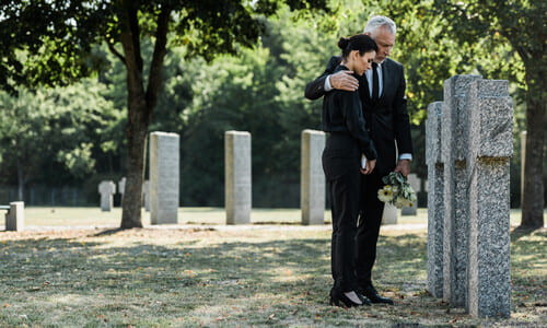 A man and a woman mourning the death of a loved one at a granite tombstone .