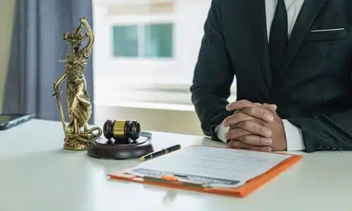 A personal injury lawyer with clasped hands resting on a table next to a statue of Lady Justice and a gavel and soundblock.