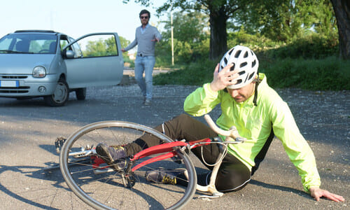 A cyclist on the ground with his bike, holding his head after a collision with a car.