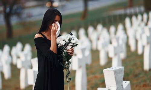 A grieving woman dressed in black crying at a loved one's tombstone.