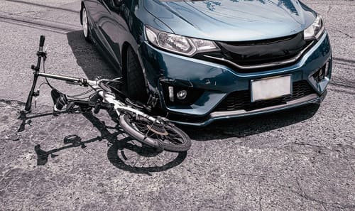 A dark green sedan after having collided and partially run over the front wheel of a folding bicycle.