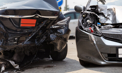 Two damaged vehicles on the side of the road displaying the damage they received from a car accident.
