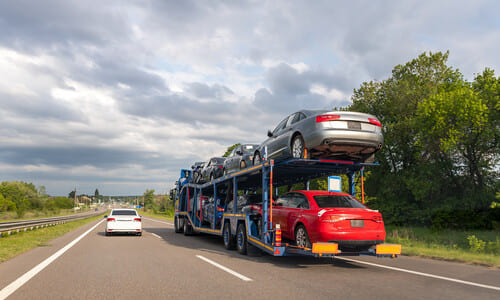 A double-deck car hauler trailer attached to a big rig on a highway next to a car.