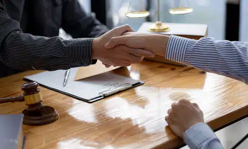 A personal injury lawyer shaking hands with a client from across a desk after coming to an agreement.