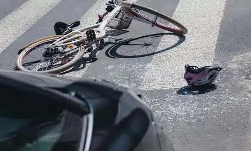 A bicycle and a cyclist's helmet lying on the a crosswalk behind a sedan after a collision.