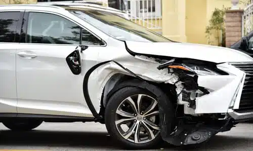 A white car with a damaged front end after a hit-and-run accident in a suburb.