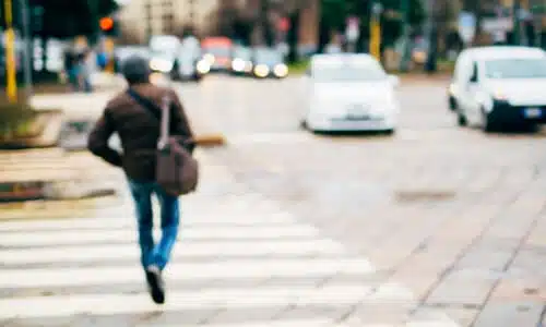 A selective focus image of a pedestrian at a crosswalk with a car about to make a turn.