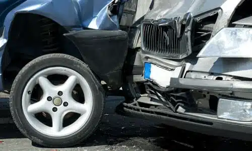 A closeup of a collision between a blue and a silver car on a road.