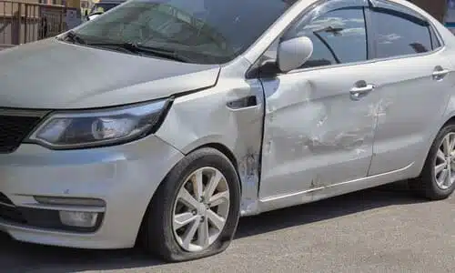 A silver-grey sedan damaged by a hit-and-run sideswipe.