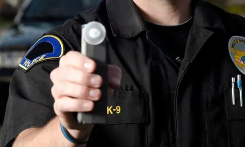 A police officer holding out a breathalyzer at chest level for a drunk driver to blow into.