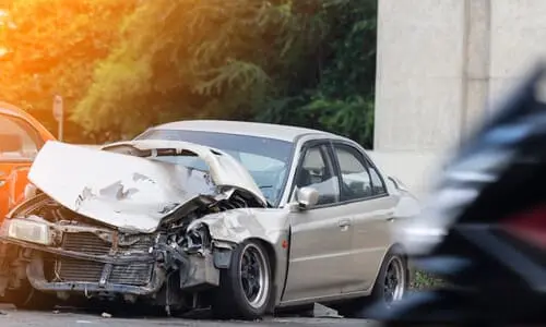 A grey sedan with a crushed engine block after a dangerous collision on the road.
