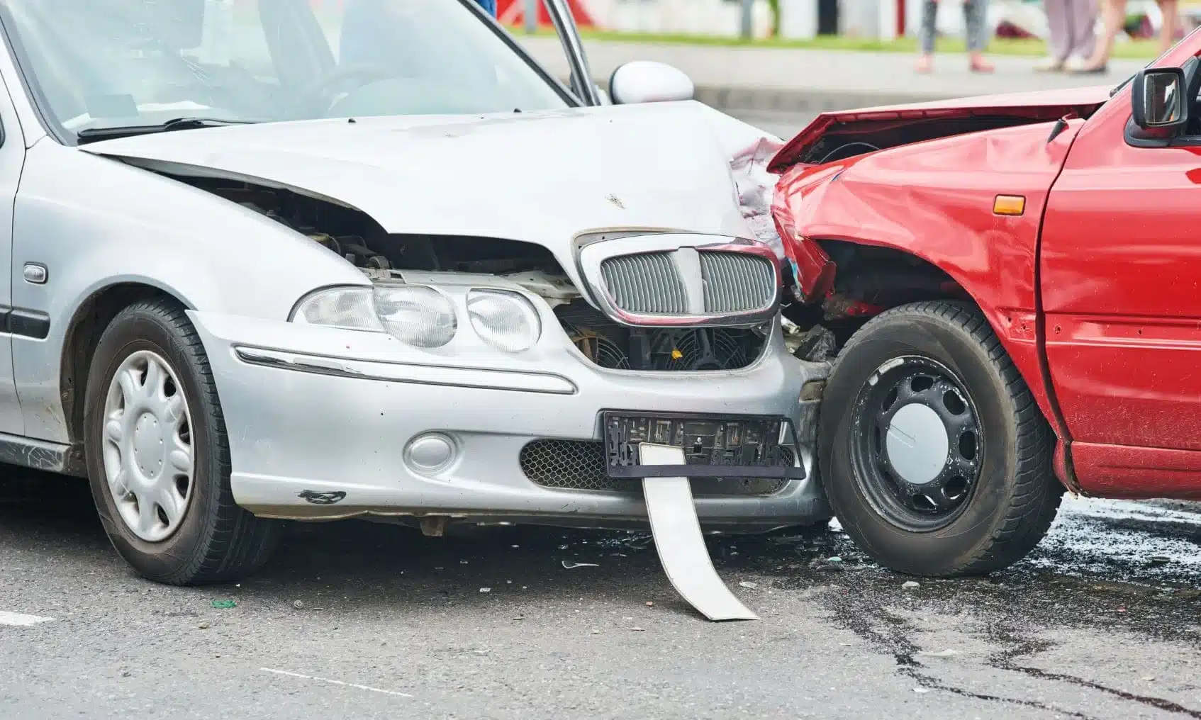 A car accident between a silver car and a red pickup truck on a road.