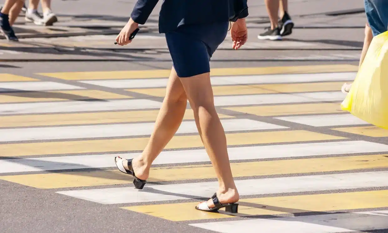 A woman in a smart attire walking across a road at a crosswalk.