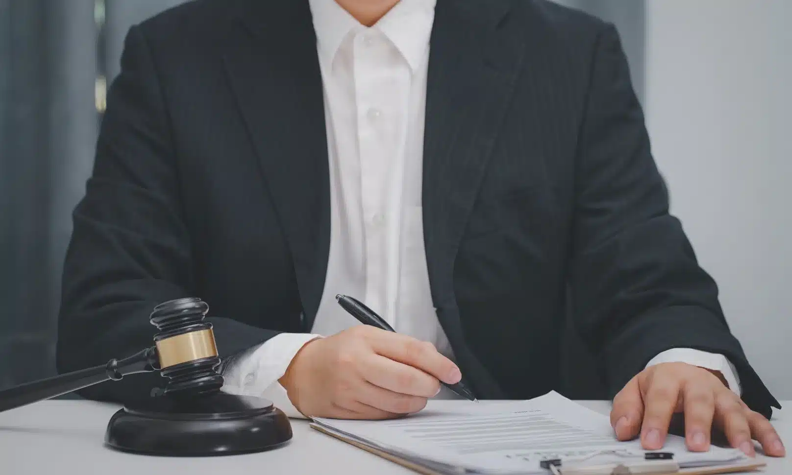 A lawyer at a desk with his hand on a clipboard with an insurance policy and noting things with his pen.